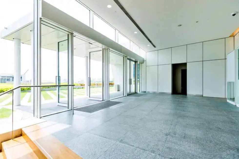 The modern building lobby, serving as a testament to eRep Industries commitment to innovation, features large glass doors, white walls, and a gray tiled floor. Sunlight streams in, highlighting the clean, minimalist design that reflects the diverse industries they serve.