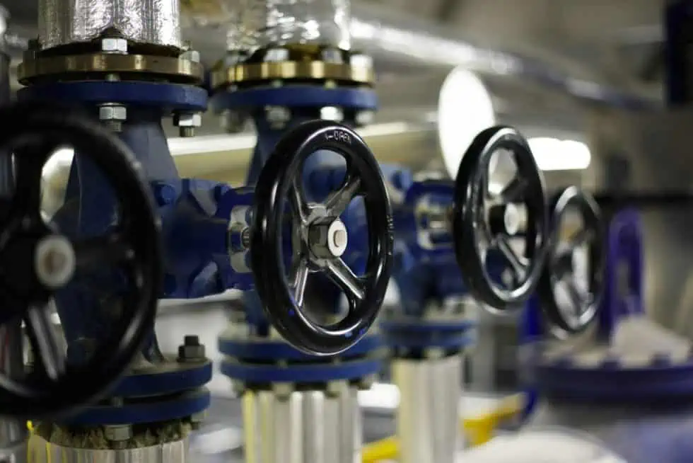 Close-up of four black-handled industrial valves connected to blue pipes in a mechanical setting, highlighting the precision and robust engineering that exemplifies the eRep Industries we serve.