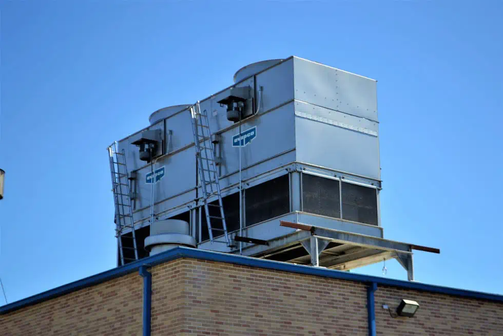 Two large industrial air conditioning units from eRep Industries sit on a flat rooftop, surrounded by safety railings and ladders, against a clear blue sky backdrop. This is just one example of the many sectors we serve with our top-notch HVAC solutions.
