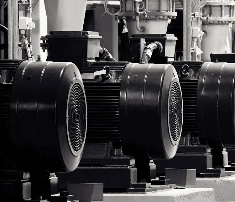 Close-up of industrial machinery in a factory setting, showcasing multiple black motors with visible air vents and connected pipes. The scene illustrates the precision akin to CPQ software for motor manufacturers, streamlining assembly and enhancing efficiency.