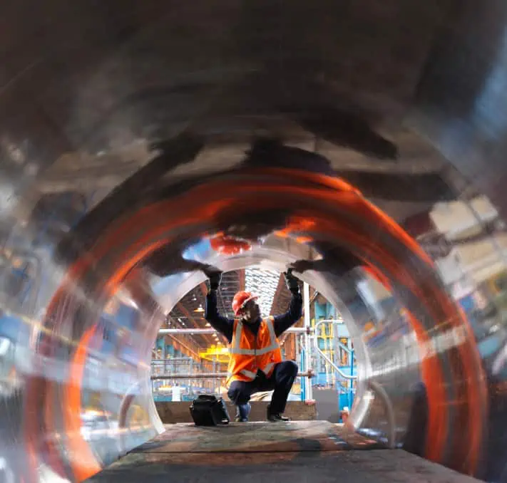 A worker in a reflective vest and hard hat examines the inside of a large cylindrical metal structure at a construction site, efficiently aligning his task with insights from the Intelliquip Project and Quote Management Portal.