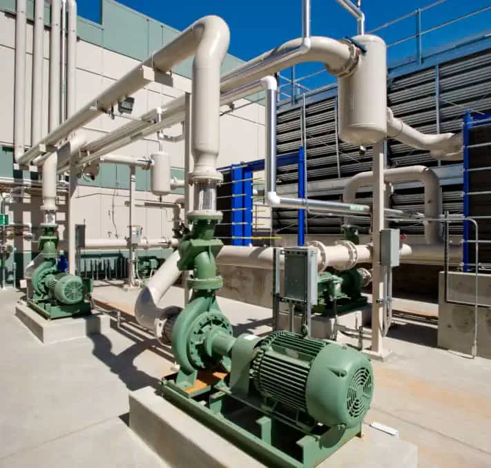 Industrial pumps and pipes in an outdoor facility showcase green machinery and a system of interconnected tubes under a clear blue sky, perfectly aligned with the precision offered by the Intelliquip Project and Quote Management Portal.