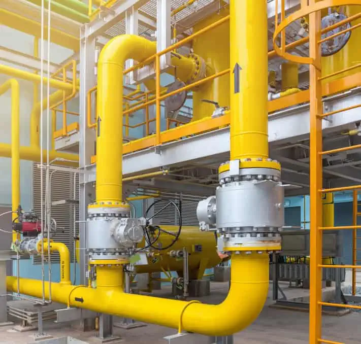 Yellow industrial pipes and valves stand prominently in a factory setting, showcasing optimal pipe performance, with metal scaffolding and platforms providing a sturdy backdrop.