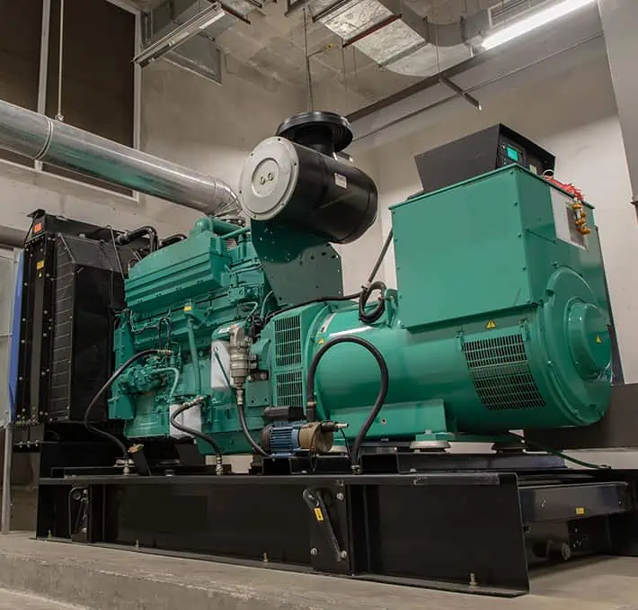 A large green industrial generator installed in a mechanical room, showcasing the intricate exposed pipes and robust metal enclosure typical of industrial machinery CPQ solutions.