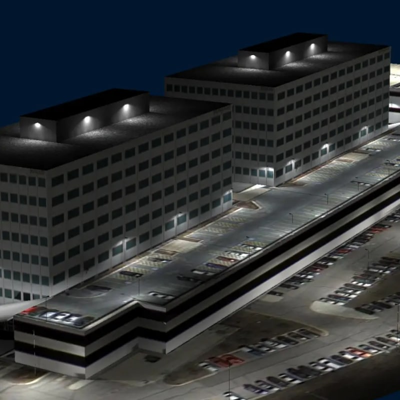 Two multi-story office buildings with illuminated rooftops, enhanced by Illuminating Engineering Software, and an adjacent multi-level parking structure filled with parked cars at night.