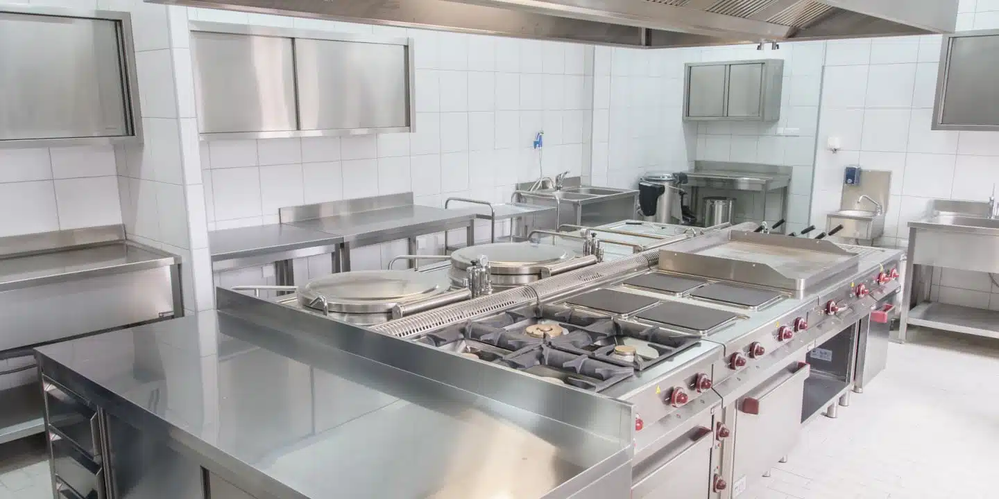 A meticulously crafted commercial kitchen features stainless steel appliances like stoves and grills, seamlessly integrating foodservice design elements against pristine white tiled walls—ideal for cooking excellence.
