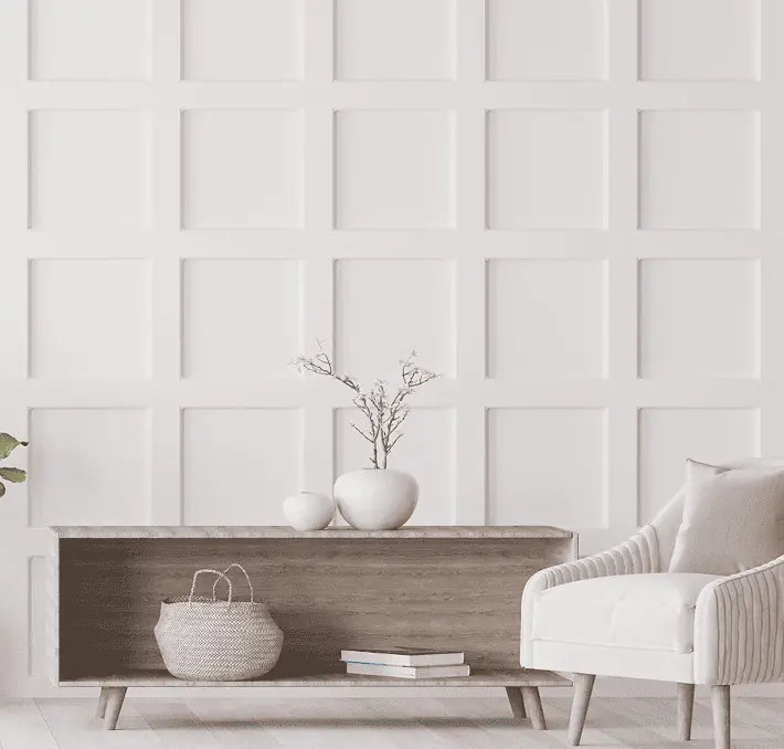 Minimalist living room with white paneled wall, wooden console table, and white armchair. Two vases with branches and a woven basket are on the table.