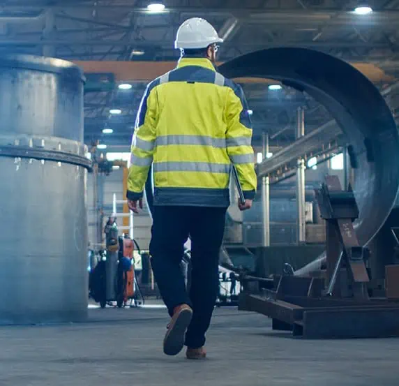 Man walking through factory with large pipes