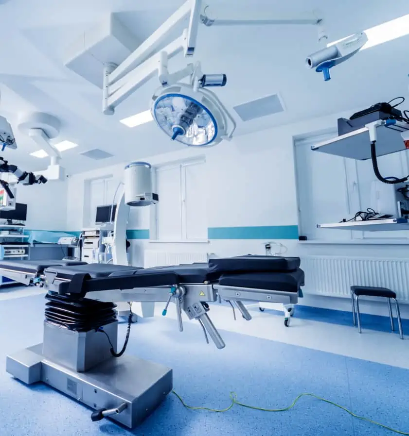 A modern, empty operating room with a surgical table and bright overhead lights showcases the precision work of biomedical and clinical engineers, as various medical equipment is meticulously arranged around the room.