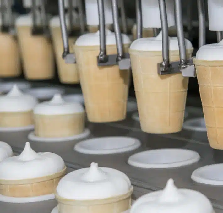 In the realm of lebensmittel, ice cream cones glide flawlessly down an automated line, being filled with vanilla soft serve. This streamlined process exemplifies efficiency akin to a getränke plm lösung, ensuring each swirl is a masterpiece.
