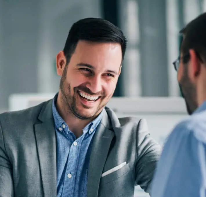 Two men are engaged in conversation, discussing the latest in product configurators. One is smiling, wearing a gray blazer and blue shirt.