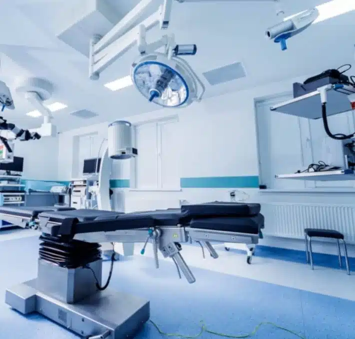 A modern medical equipment planning operating room showcases expertly installed medical equipment, featuring surgical tools and overhead lights. The space is defined by blue and white walls and floors, with various machines and monitors seamlessly integrated for optimal care.