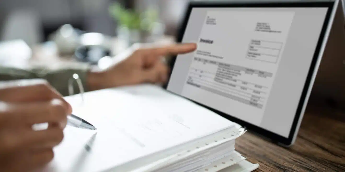 A person is reviewing an invoice on a tablet with a pen in hand, pointing at a detail related to the TCO of biomedical devices on the screen.