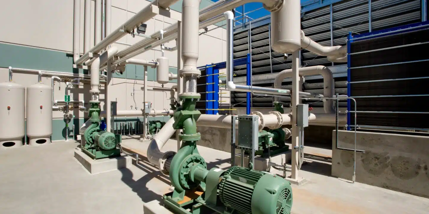 The industrial facility exterior features a complex piping system, pumps, and storage tanks, all mirrored in a cutting-edge digital twin for fluid management against the backdrop of a clear blue sky.