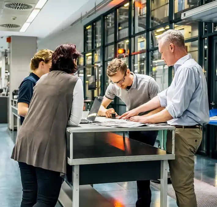Four colleagues in a modern office setting gathered around a table, meticulously focused on documents and a laptop, epitomizing CPQ success as they streamline their sales process.