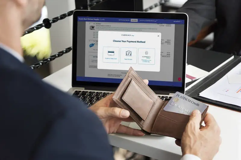 A person holds a wallet and a credit card while facing a laptop screen displaying Choose Your Payment Method, with online payment options like AQ Pay clearly visible.
