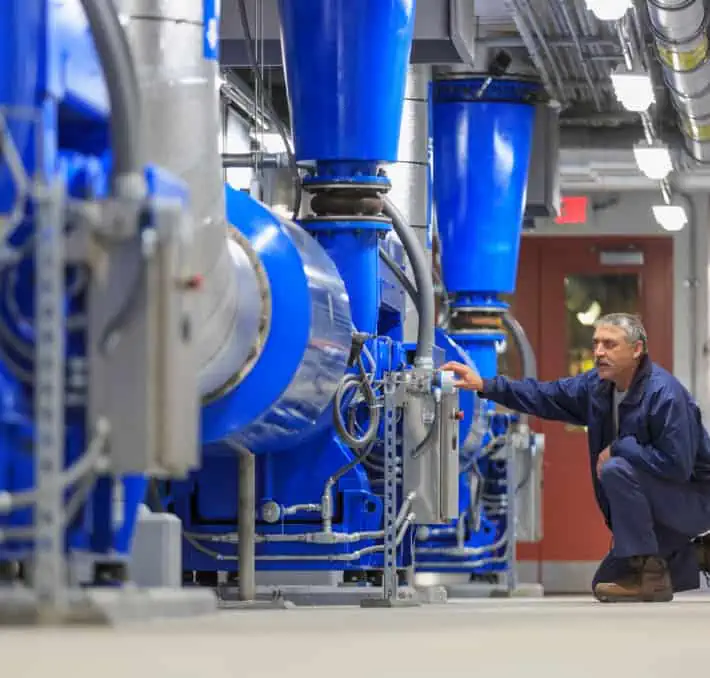 A person inspects large blue machinery in an industrial setting, utilizing fluid modeling software to ensure optimal performance.