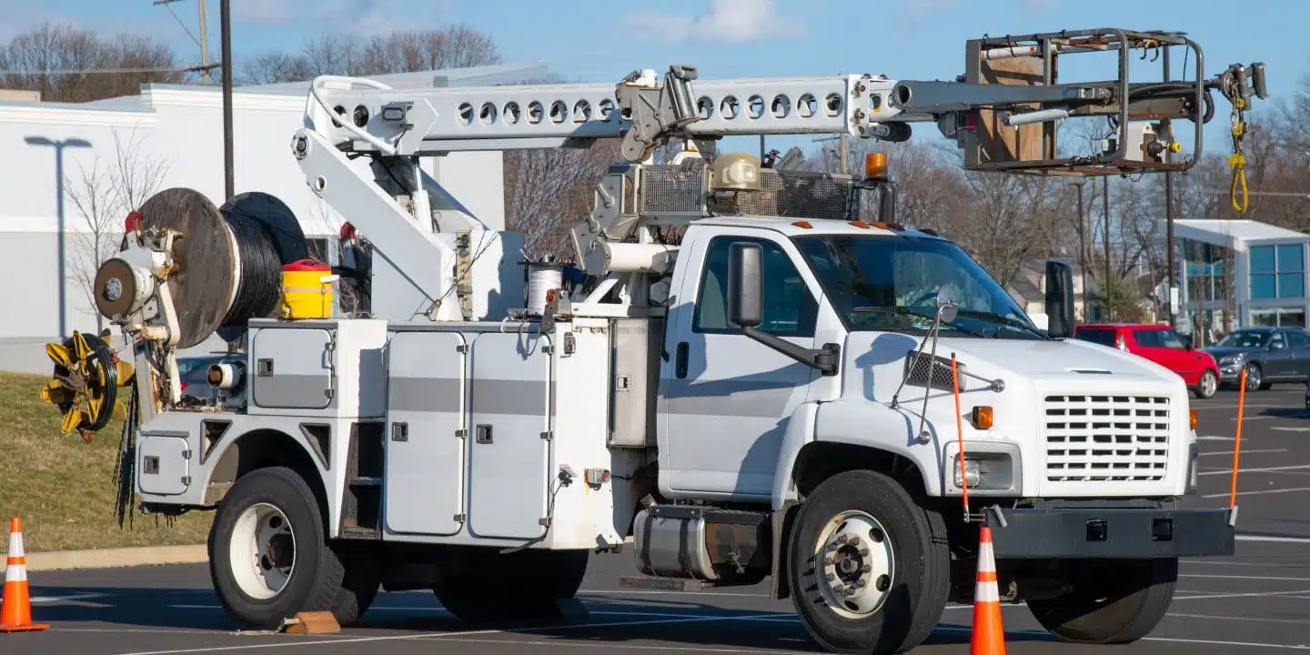 A specialty vehicle manufacturing marvel, this utility truck features an elevated boom lift in a parking lot, expertly surrounded by traffic cones.