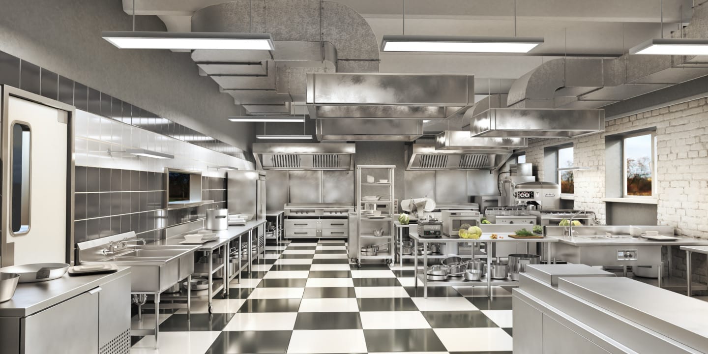 Commercial kitchen with stainless steel appliances and countertops, checkered floor, industrial lighting, and high ceilings. Designed using cutting-edge commercial kitchen design software, cooking utensils and ingredients are arranged neatly for optimal efficiency.