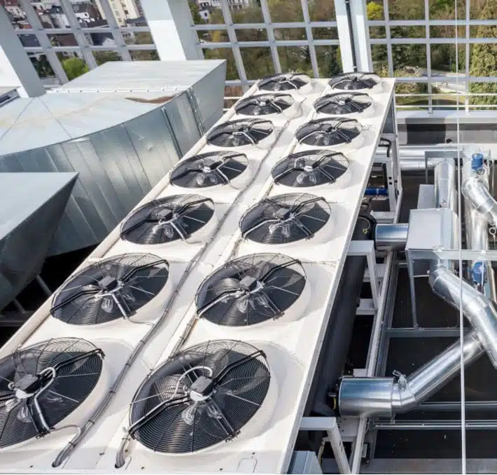 A rooftop view showcases large industrial air conditioning units, perfectly illustrating the intricacies of CPQ in the HVACR industry, with multiple fans and metal ducts set against a backdrop of windows and cityscape.