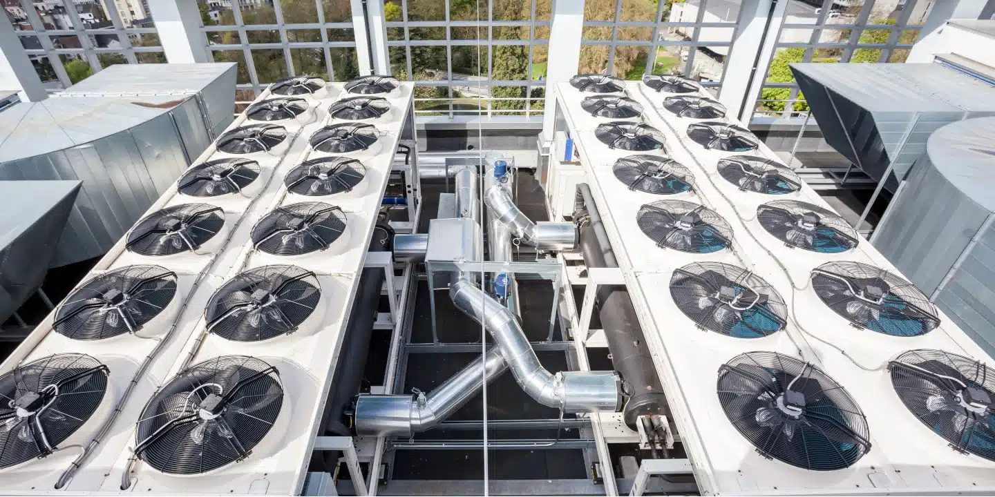 A rooftop view of industrial HVAC units with multiple fans and connected ductwork, set against a background of windows, exemplifies the efficiency driven by CPQ in the HVACR industry.