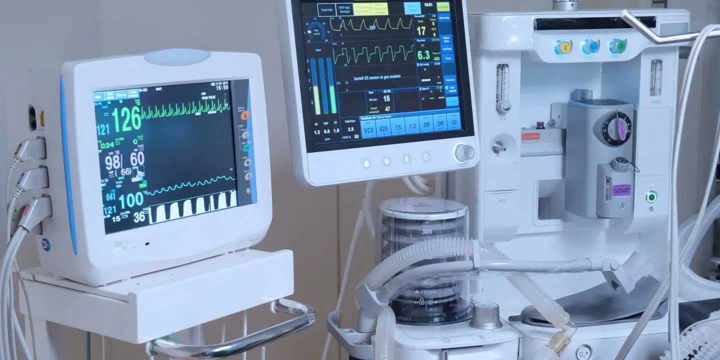 In a hospital setting, biomedical devices including monitors display vital signs and respiratory data, complemented by an anesthesia machine with intricate tubes and dials.