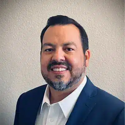 A smiling man with short dark hair and a beard, wearing a dark suit jacket and white shirt, stands against a plain light-colored wall. His confident stance echoes the professional atmosphere of ProFood Welt.
