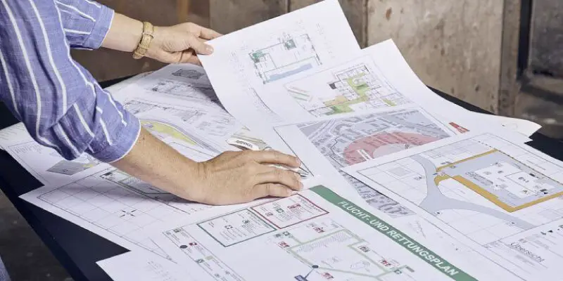 A person meticulously reviews architectural and emergency exit plans spread across a table, ensuring every detail aligns with the extinguishing water supply system for optimal safety.