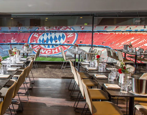 Tables set for dining overlook a football stadium with red seats and a large FC Bayern Munich logo visible in the stands.