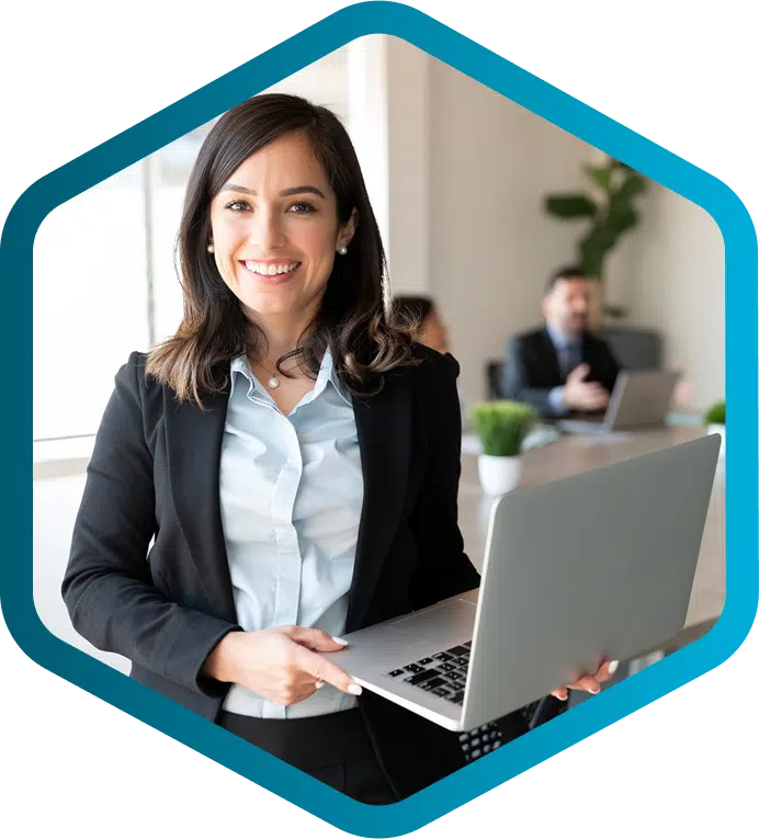 Woman in business attire holding a laptop and smiling, while two colleagues discuss HVAC equipment manufacturers CPQ solutions at a conference table in the background.