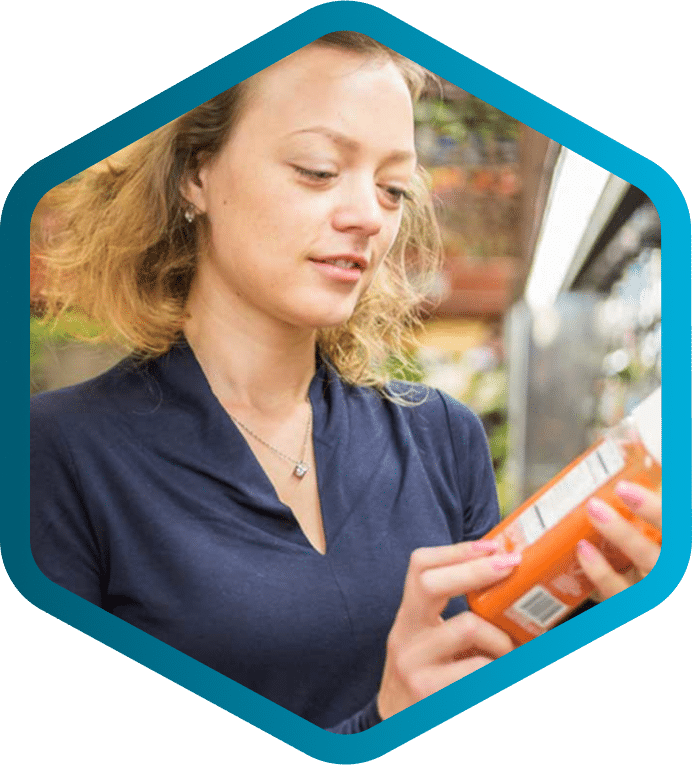 A woman in a navy blue top reads the label on a jar in a grocery store aisle, highlighting how PLM for food and beverage ensures accurate product information.