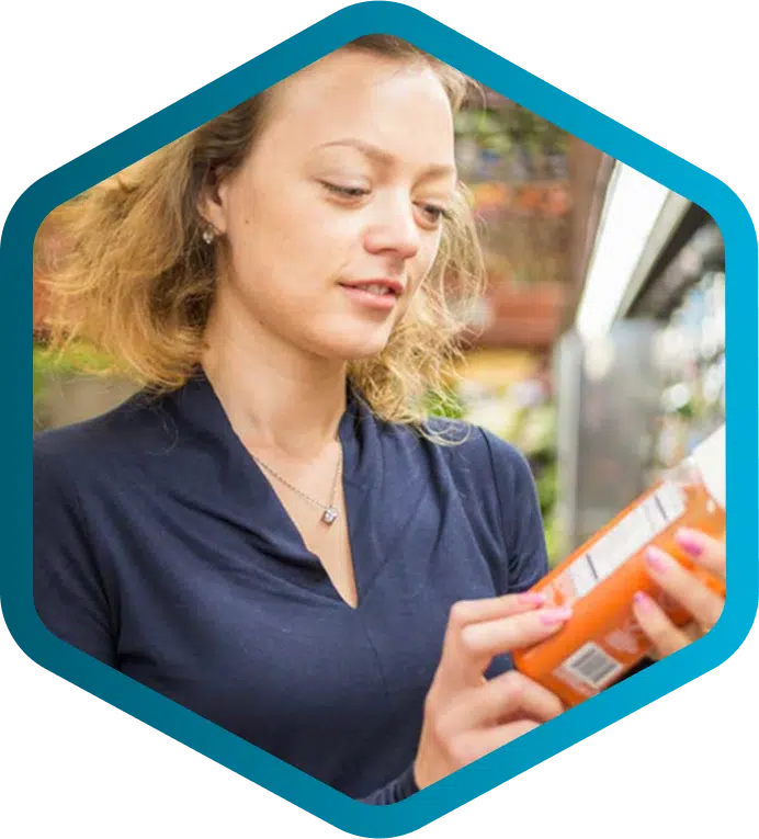 A woman in a navy blue top reads the label on a jar in a grocery store aisle, highlighting how PLM for food and beverage ensures accurate product information.