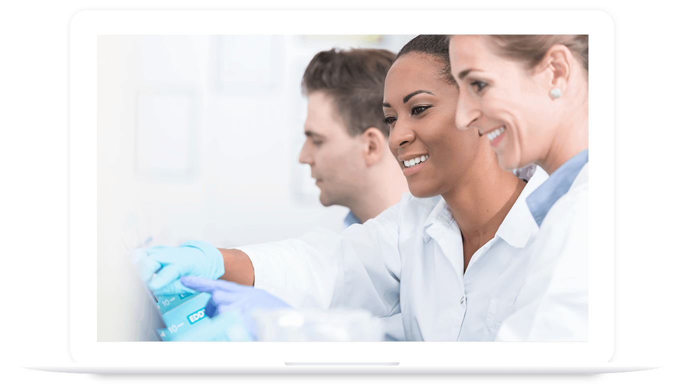 Three scientists wearing lab coats and gloves work together in a laboratory, focusing on an experiment or research task involving PLM for food and beverage, displayed on a laptop screen.