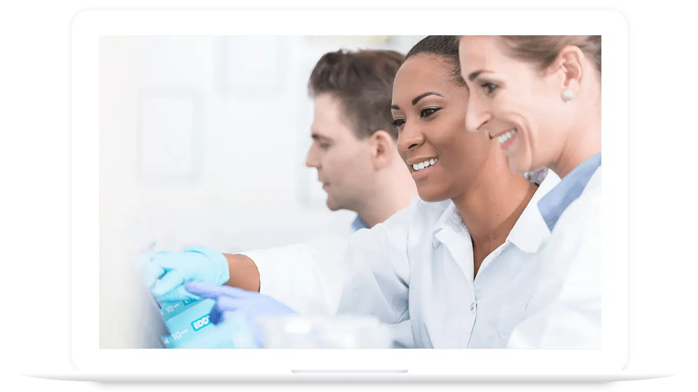 Three scientists wearing lab coats and gloves work together in a laboratory, focusing on an experiment or research task involving PLM for food and beverage, displayed on a laptop screen.