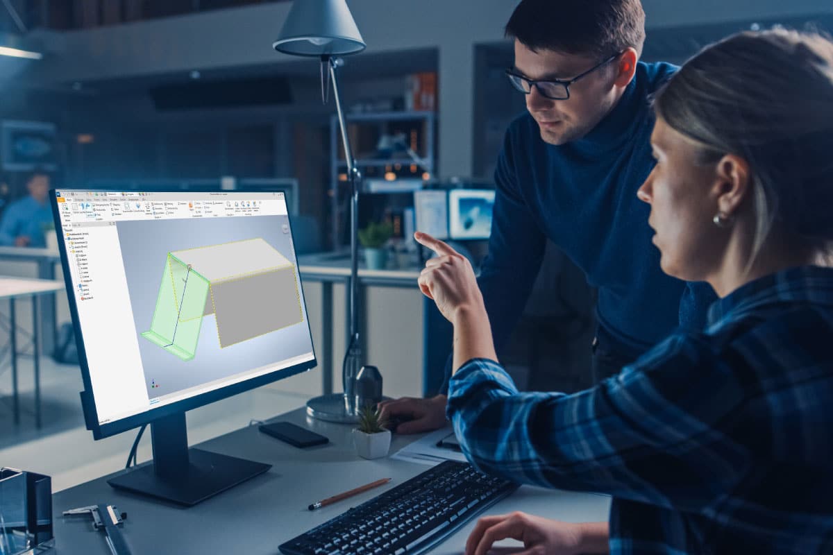 Two people look at a computer monitor displaying a 3D design in CAD software, discussing the structural model on the screen in an office setting.