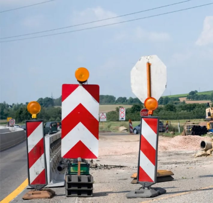 Three road barricades with orange warning lights and red-white chevron patterns block a section of road; a faded stop sign is visible in the background—perfect inspiration for CAD drawing and design software projects.