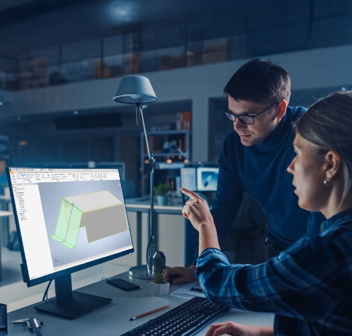 Zwei Personen in einem Büro diskutieren über ein 3D-Modell einer Metallkonstruktion, das auf einem Computermonitor angezeigt wird, wobei eine Person auf den Bildschirm zeigt.