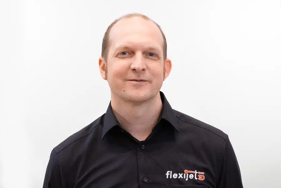 A man with short hair wearing a black collared shirt with a flexijet logo stands against a plain white background.