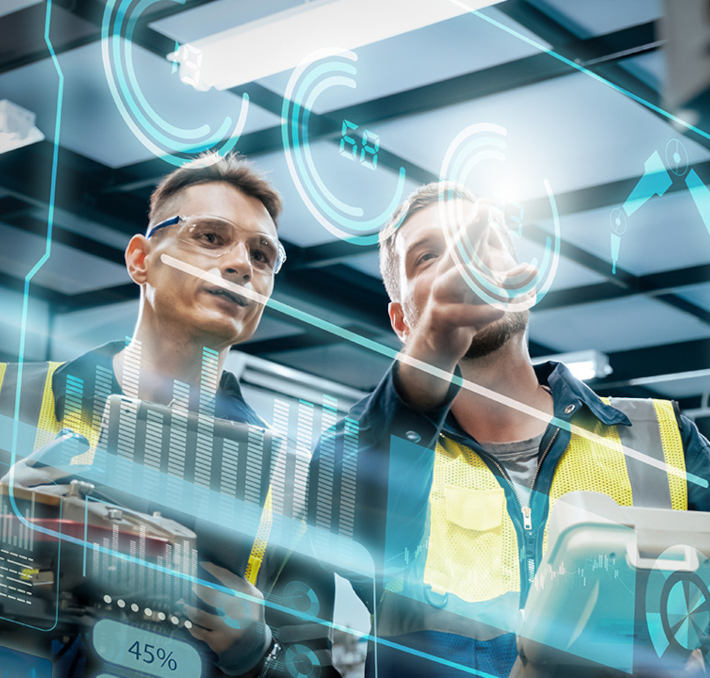Zwei Arbeiter in Sicherheitswesten und Schutzbrillen bedienen in einer modernen Industrieumgebung Maschinen, die mit digitalen Daten und Schnittstellengrafiken überlagert sind.